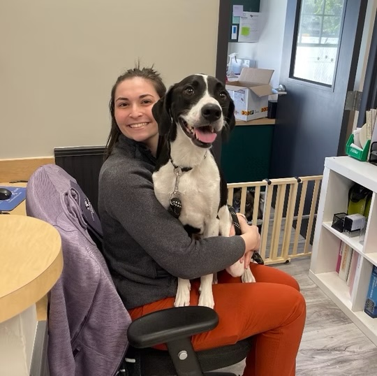 Smiling veterinary staff member holding a happy black and white dog at a veterinary clinic in Bluffton
